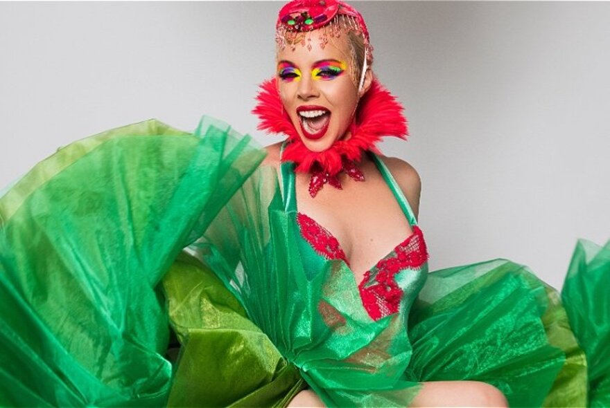 A woman in a green and red cabaret costume with colourful makeup; green taffeta material bunched around her.