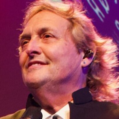 Singer with longish blond hair, backlit by a screen.