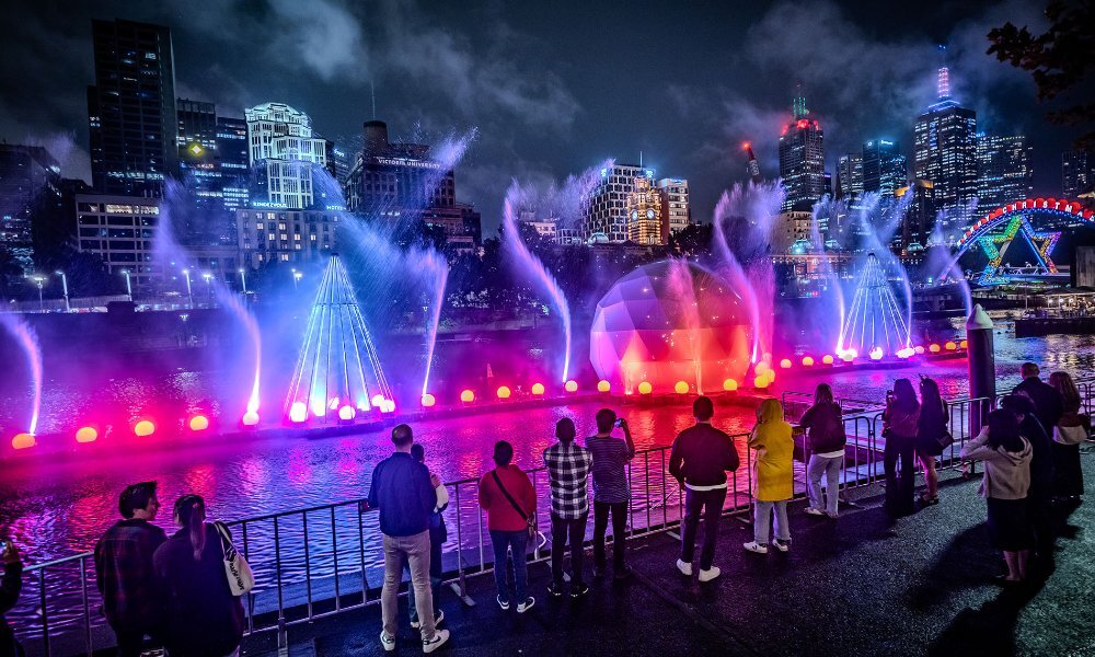 People watching a colourful river with water spouts.