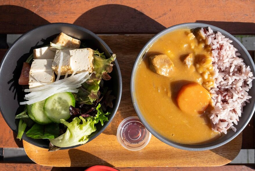 A bowl of curry with rice and a bowl of salad on an outdoor cafe table.