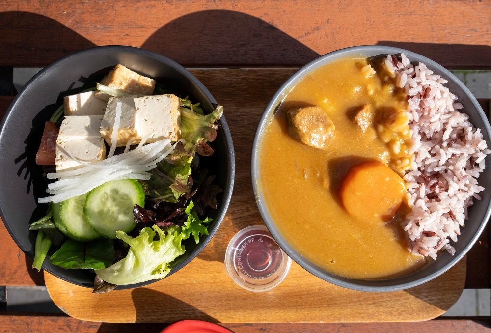 A bowl of curry with rice and a bowl of salad on an outdoor cafe table.