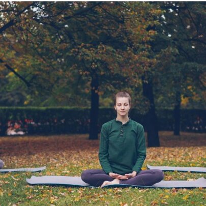 Three people seated on yoga mats in meditation poses in a garden setting with autumn leaves.