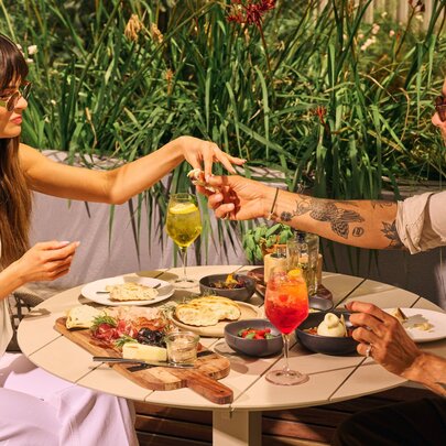A beautiful young couple enjoying cocktails and share plates at an outdoor garden bar.