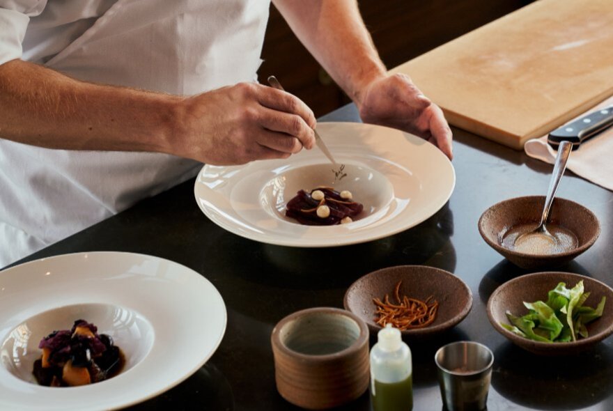 A chef garnishing a dish using fine tweezers, in a commercial kitchen.