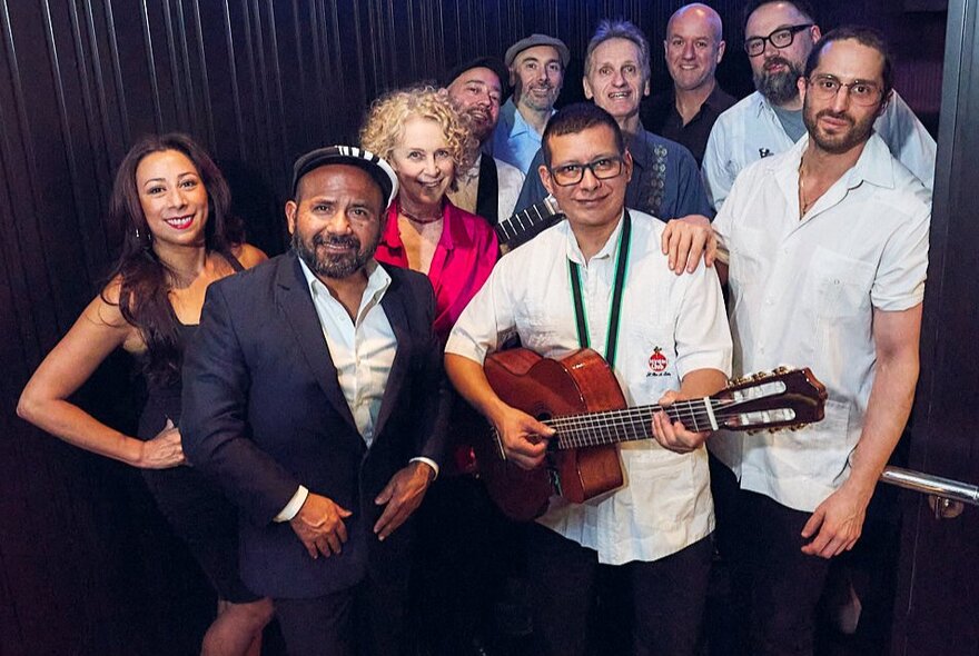 A band of musicians and singers smiling at the camera backstage.