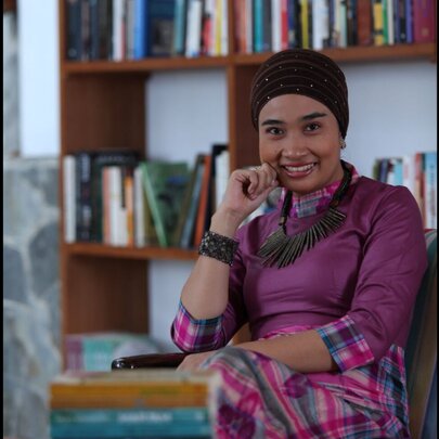 Indonesian novelist and sociologist Okky Madasari posing in front of a bookshelf.