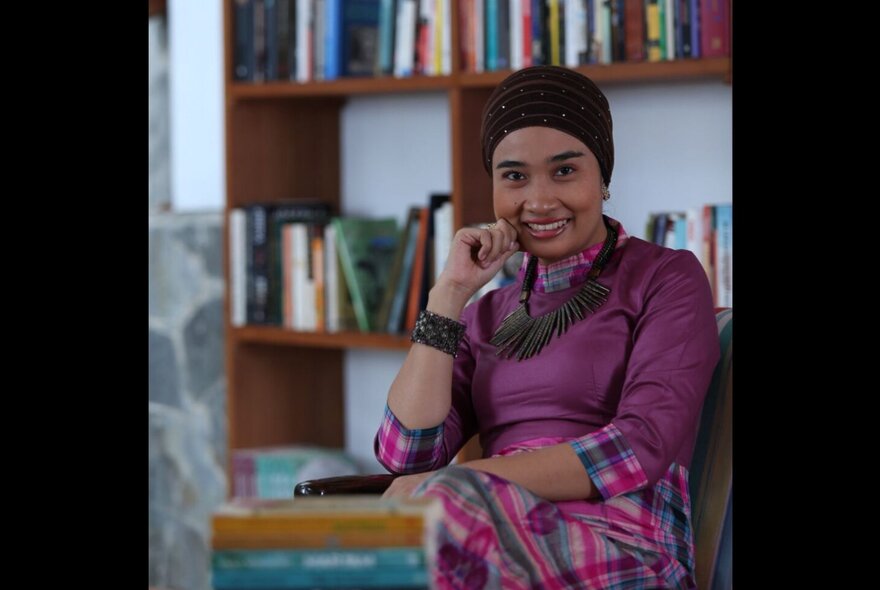 Indonesian novelist and sociologist Okky Madasari posing in front of a bookshelf.
