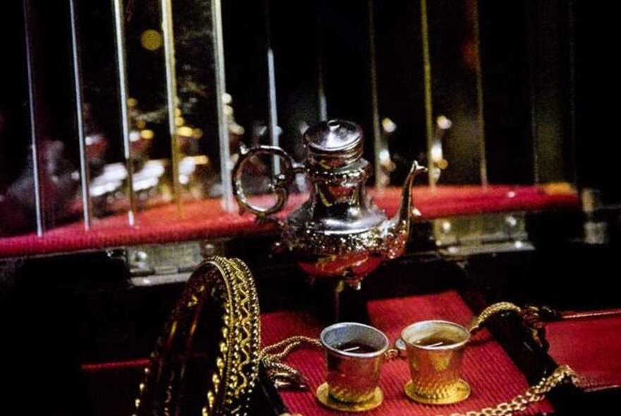 Turkish coffee in two small gold cups, with a coffee pot on the table, interior scene.