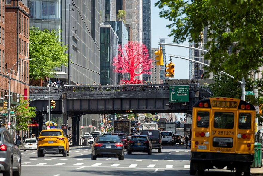 Looking at an American city with a yellow schoolbus and a railway overpass. 