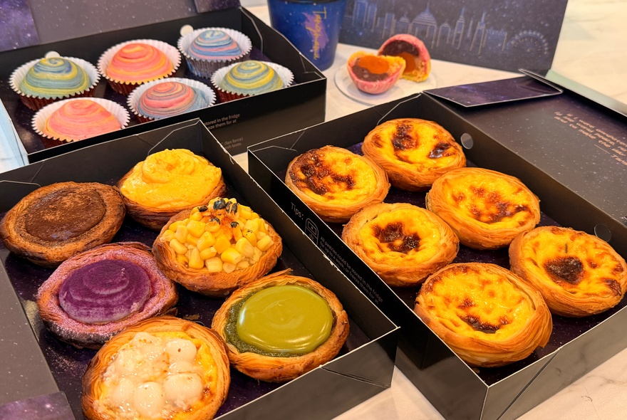 Gift boxes each containing a selection rainbow coloured pastries and egg custard flaky tarts.