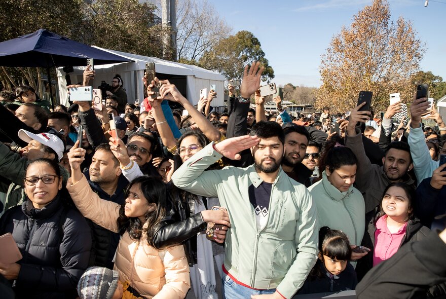 A large crowd of people outdoors, some holding up phones to take pictures. 
