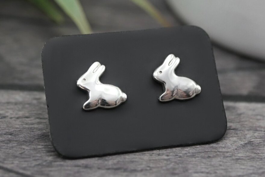 Silver rabbit-shaped earrings on a black stand.