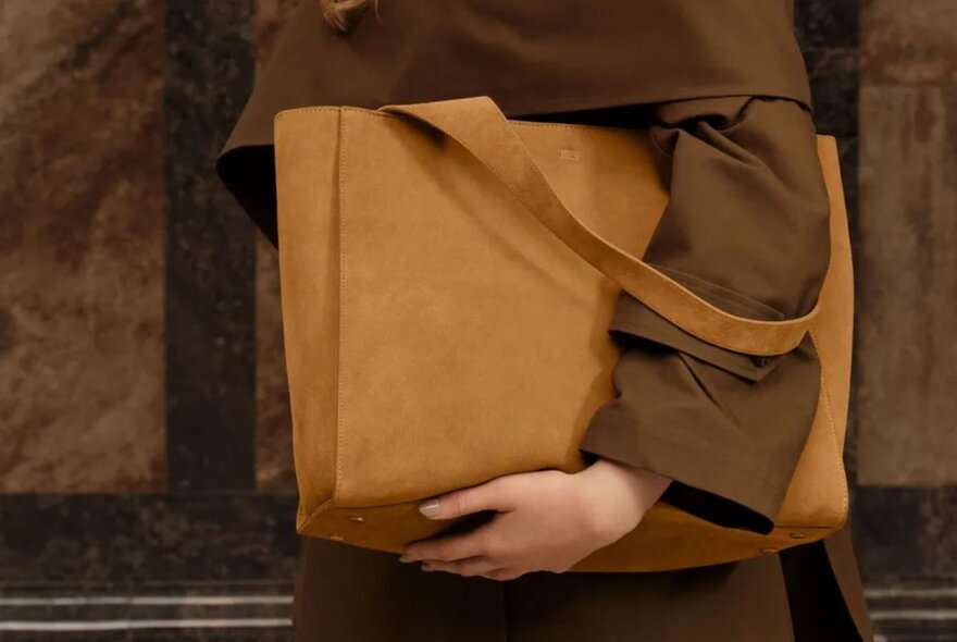 A person is holding a brown suede bag