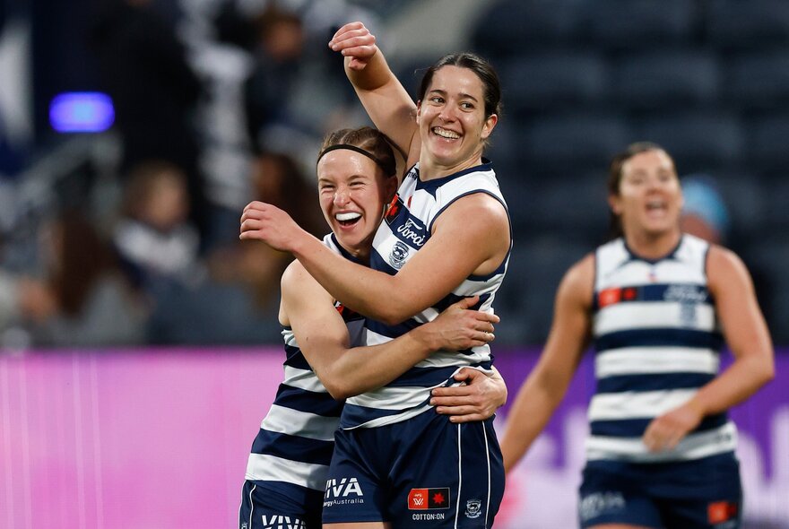 Geelong AFLW players celebrating on the football field, two of them hugging each other.