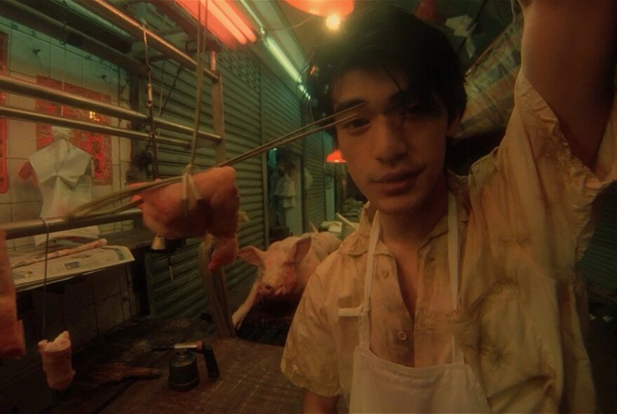 A still from the film Fallen Angels, of a young man in a Hong Kong alleyway, behind him is a pig carcass.