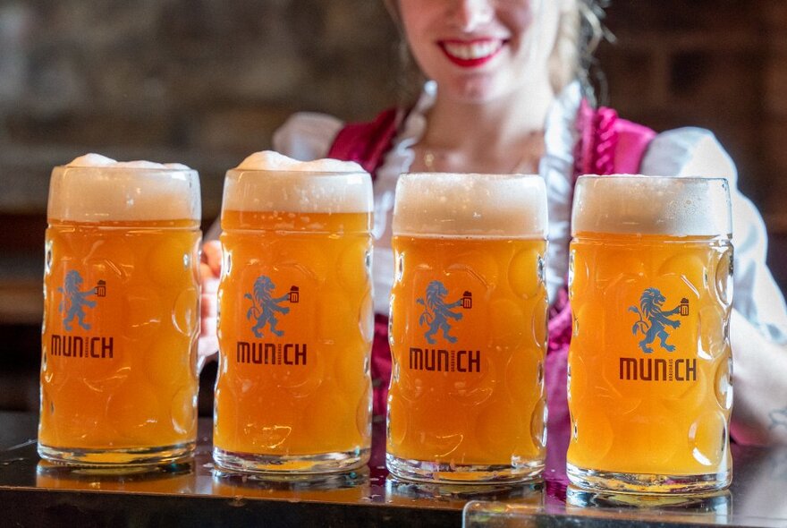 A close-up of a waitress serving four steins of beer.