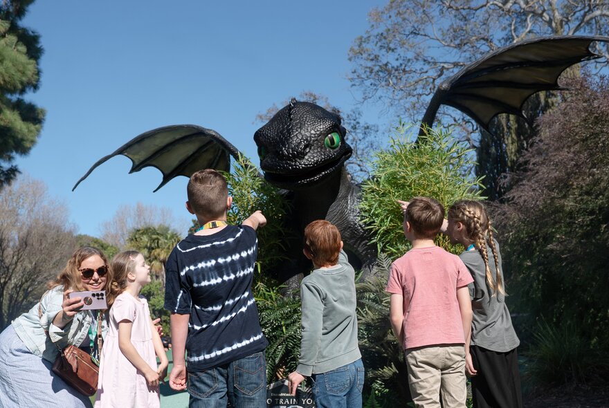 Children standing in front of a gigantic black dragon with wings up. 