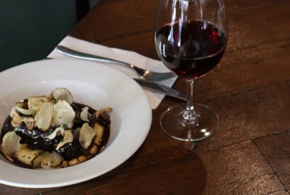 Dish of food with cutlery and glass of red wine.