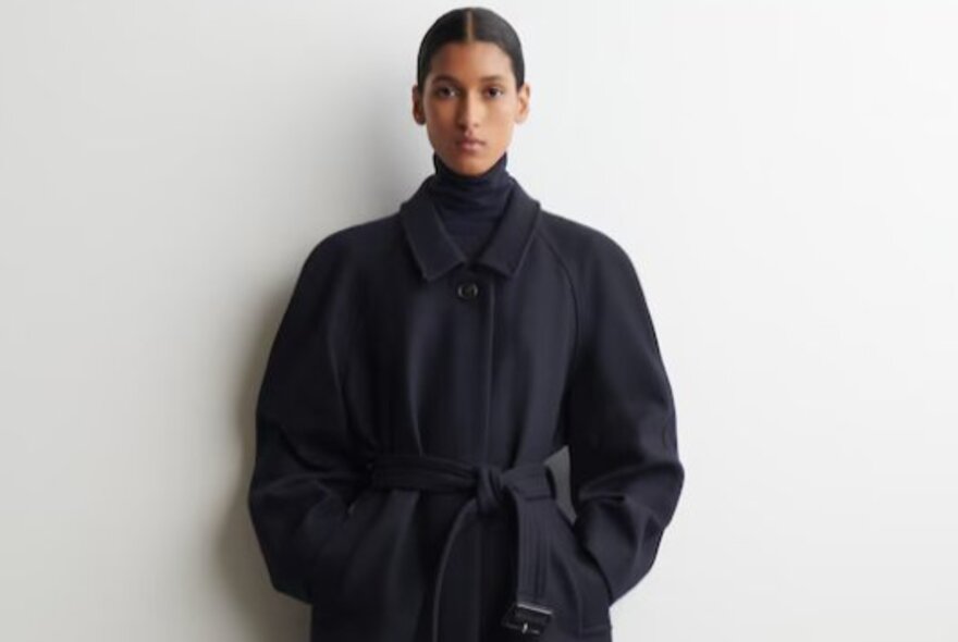 A model wearing a black wool coat with a belt. 