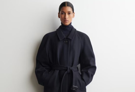 A model wearing a black wool coat with a belt. 