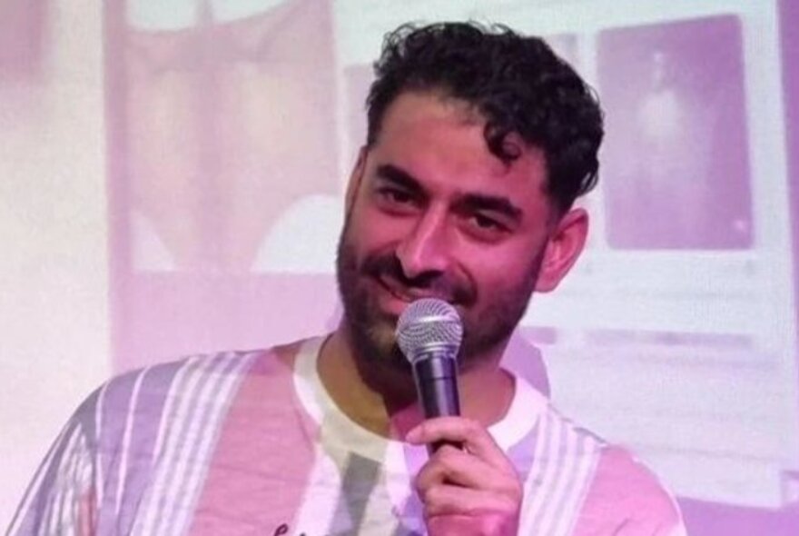 A man smiling while tilting on the side and holding a microphone.