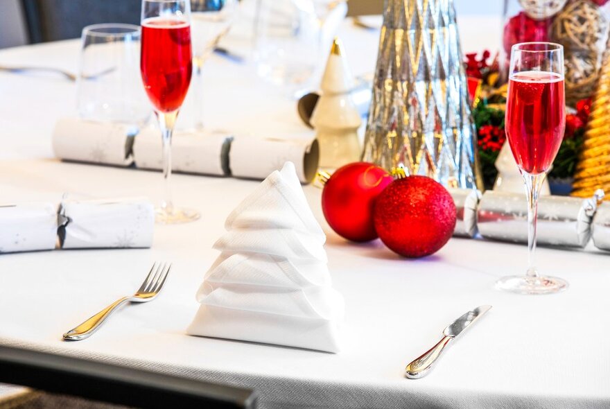 A table set for Christmas with baubles, Christmas ornaments and a serviette in the shape of a Christmas tree.