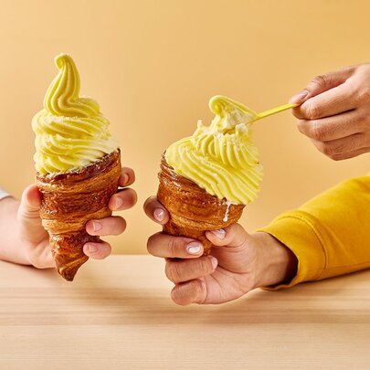 Two hands holding yellow soft serve in a pastry cone. 