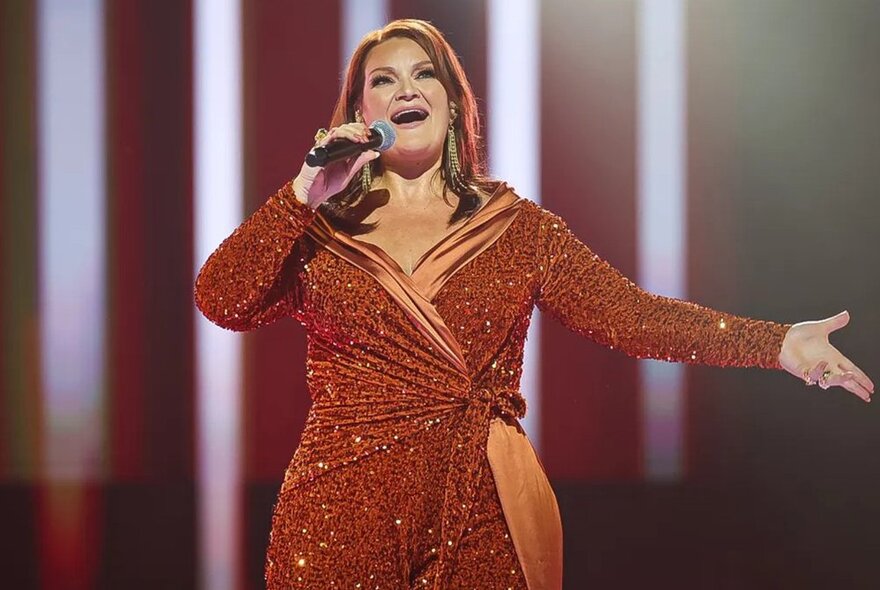 Icelandic Eurovision star Hera Björk, in bronze wrap dress, singing with arm outstretched.