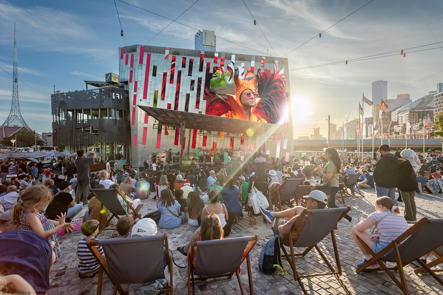 People on deck chairs watching a movie in Fed Square on a large screen.
