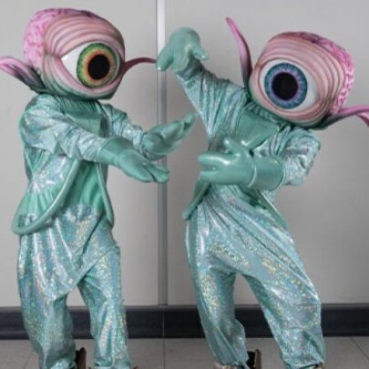 Performers in pale blue sparkly suits wearing giant eyes as heads.
