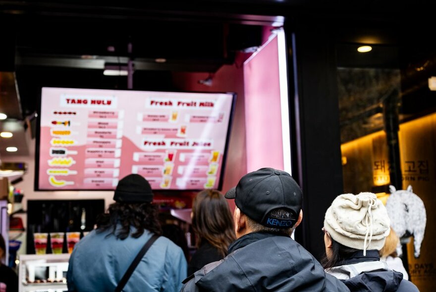 People queuing at a dessert bar, looking at a pink menu screen.