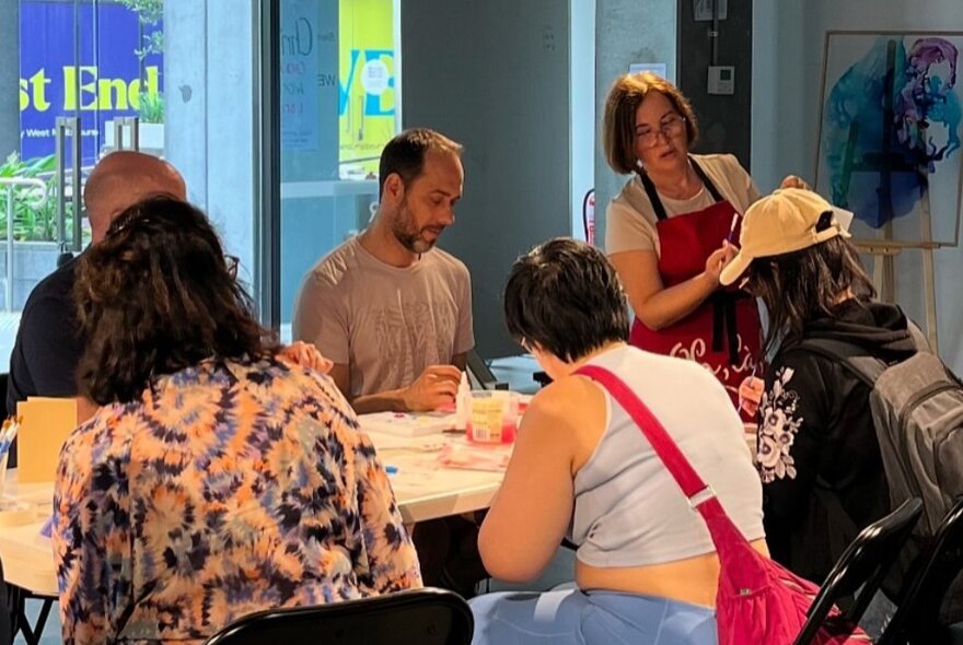 Participants taking part in a painting workshop inside a studio, with a tutor standing at the front of the group.