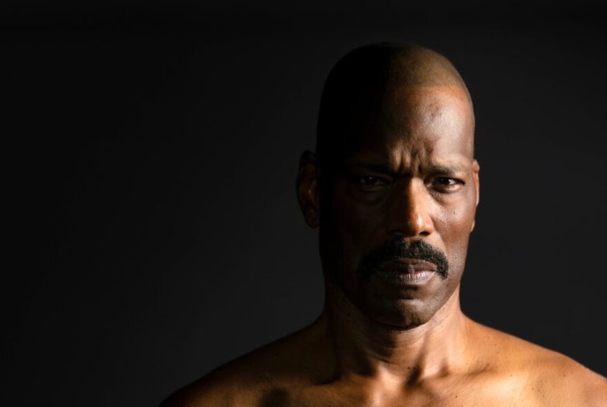 Dark headshot of an actor playing Othello, light only on half of his face.