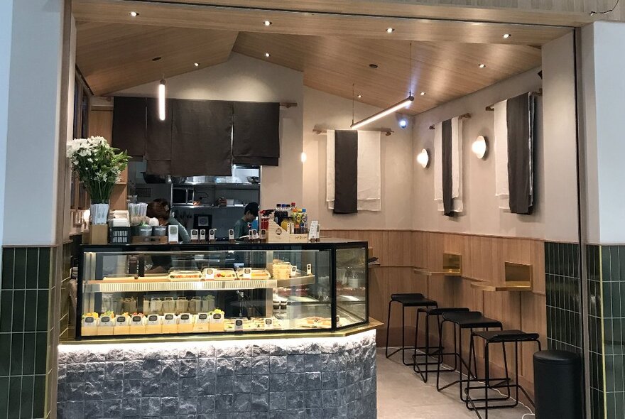 A sushi counter at a small Japanese cafe with tiny wall-fixed tables and stools.