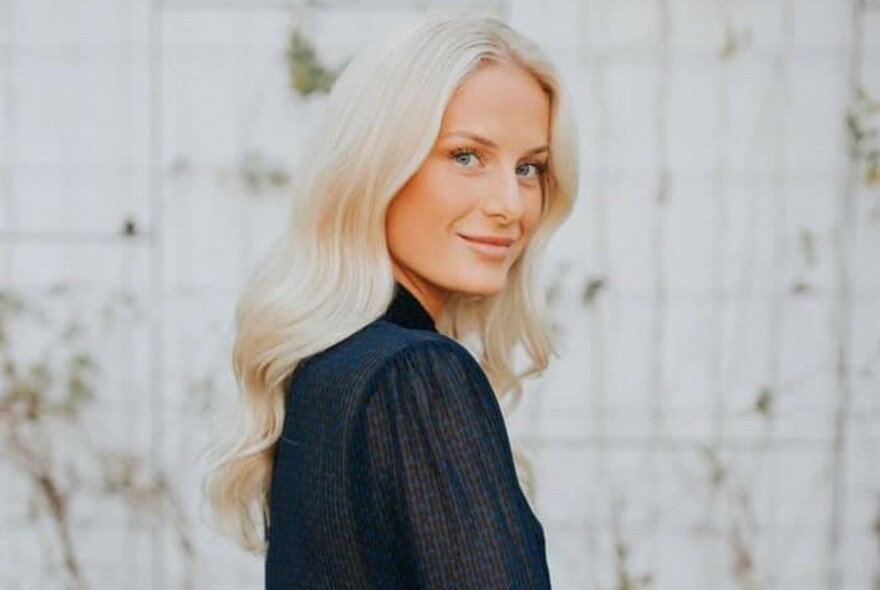 Smiling woman with long blonde hair in a black top against a white background.