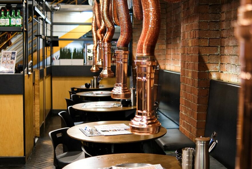 Interior of White Tomato Korean restaurant showing small round tables with chairs, and hanging mini copper extractor fans above each table.