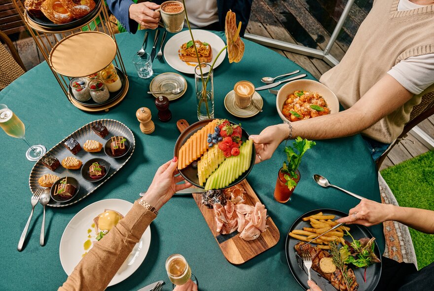 Hands reaching to take food from plates on a green table. 