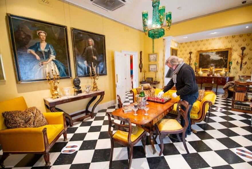 A man exploring an old-fashioned dining room with a chequerboard floor.