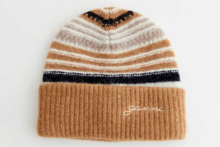 A striped brown, black and white cuffed beanie with a Ganni logo.