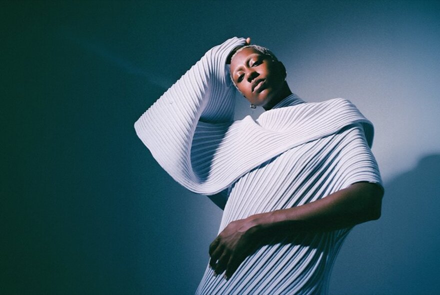 Musician Anaiis, who is looking directly at the camera while wearing a white, pleated, architectural garment with a large, voluminous collar.