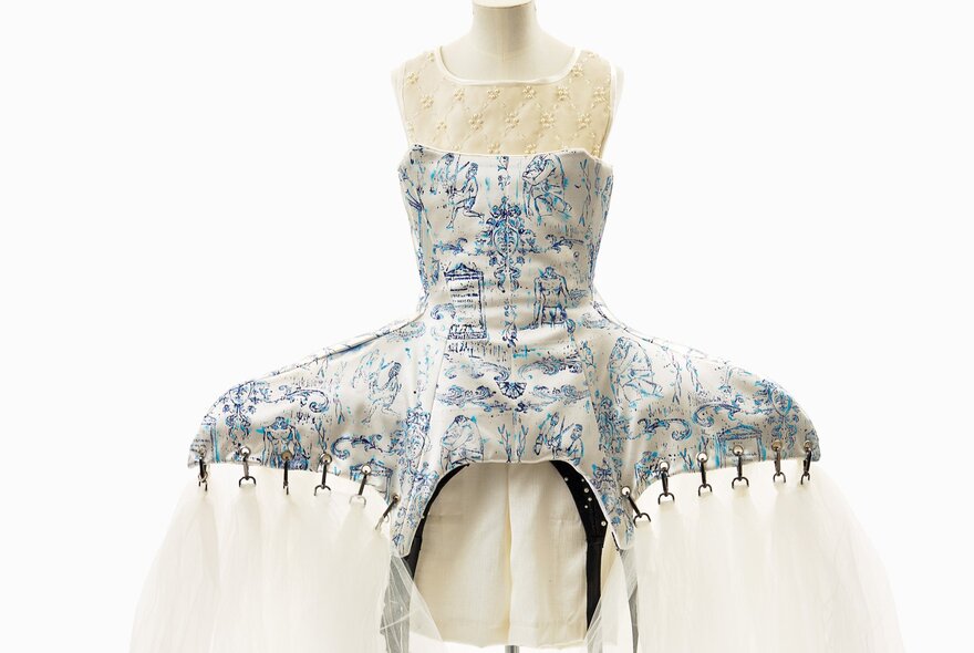 A decorative dress or sculptural piece, featuring a structured bodice with a blue and white patterned design and a sheer, flowing skirt.