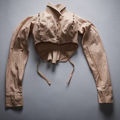 A discarded Victorian blouse with long sleeves and a high collar, placed on a grey surface.