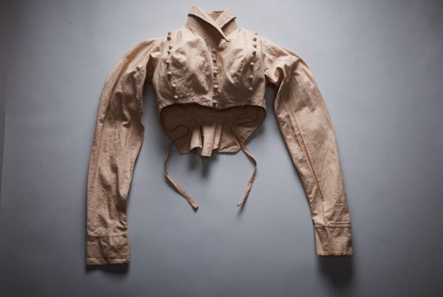 A discarded Victorian blouse with long sleeves and a high collar, placed on a grey surface.