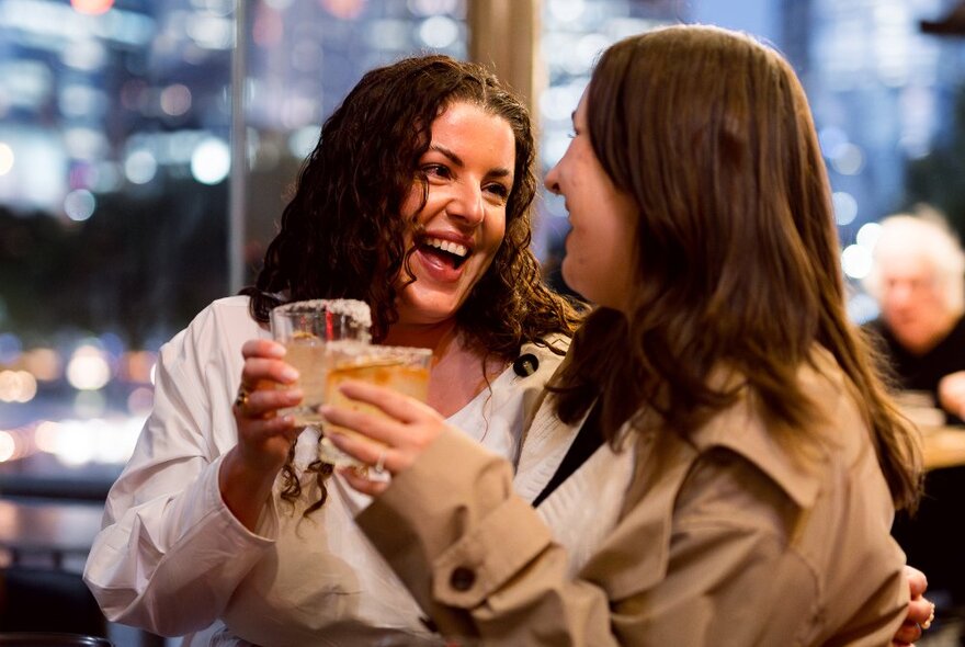 Two friends enjoying a laugh as they clink glasses. 