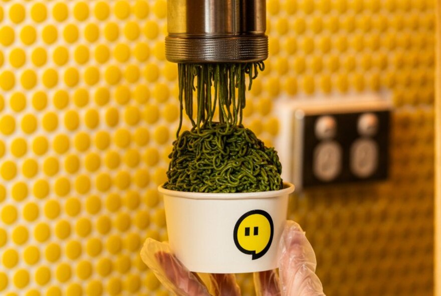 A machine making Mont Blanc squiggles on top of a gelato cup. 