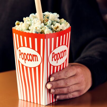 Someone holding a red striped box of movie popcorn with a straw in it. 