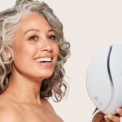 Woman with long wavy grey hair, holding a sculptured face mask.