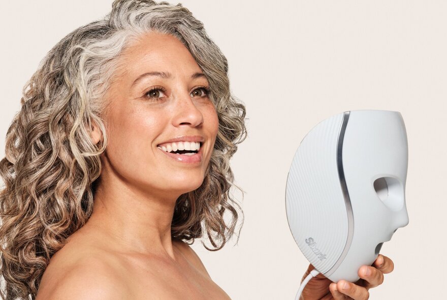 Woman with long wavy grey hair, holding a sculptured face mask.