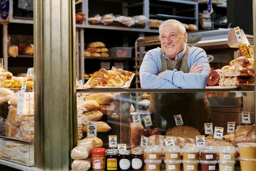 Smiling vendor selling a range of pastries, dips and spreads at Queen Victoria Market.