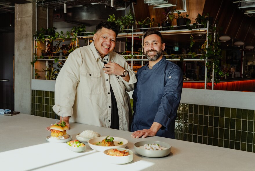 Two men standing next to an array of dishes on a counter.
